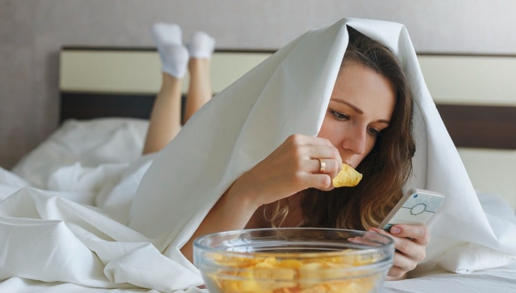 Donna mangia patatine a letto