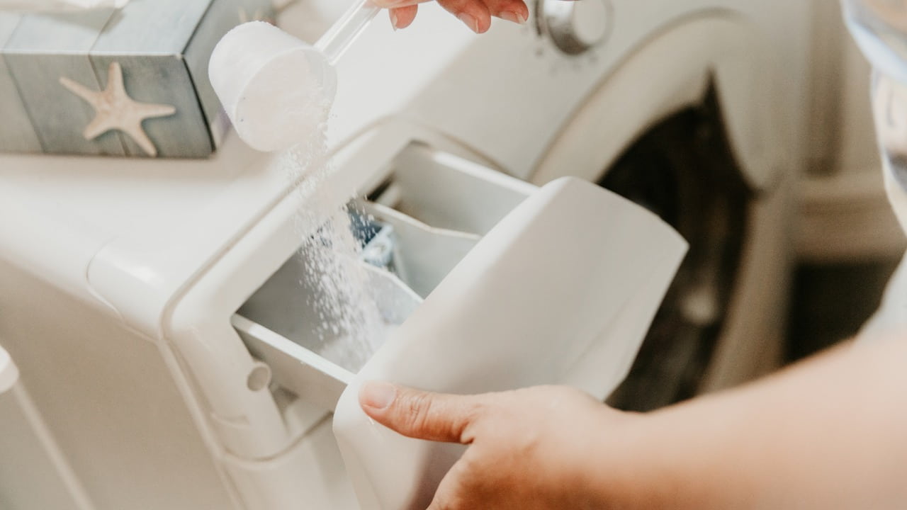 Hand schüttet Waschmittel in die Waschmaschine